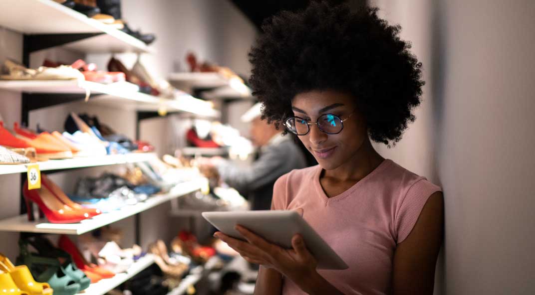 Woman reads tablet next to a rack of shoes