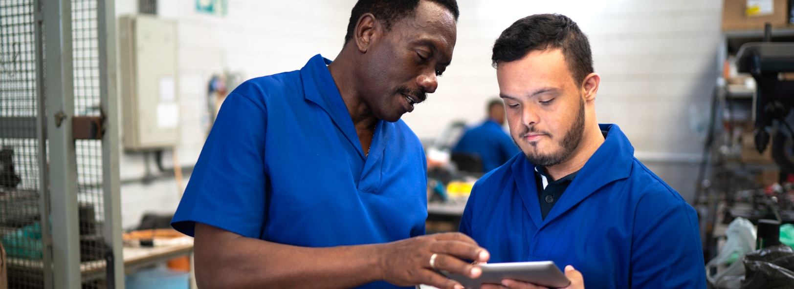 Two men read tablet in industrial environment