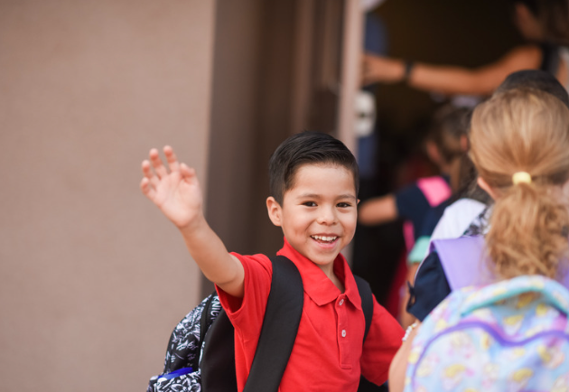 elementary student with backpack waving his arm
