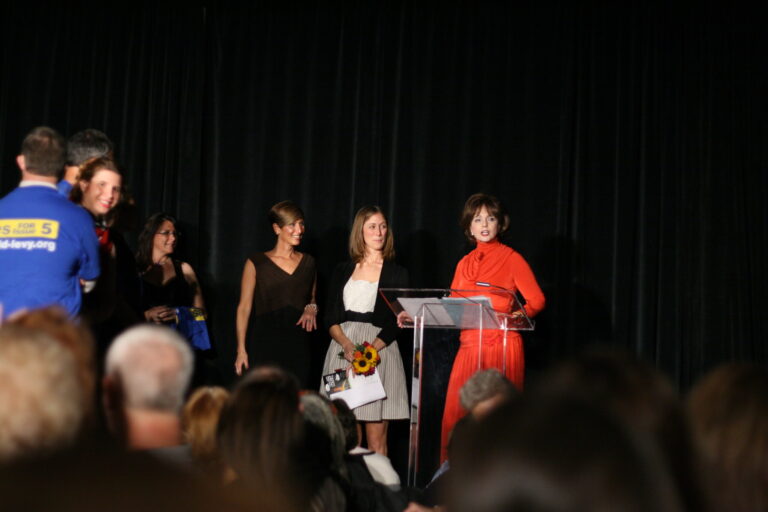 Woman in red dress speaking at podium on stage