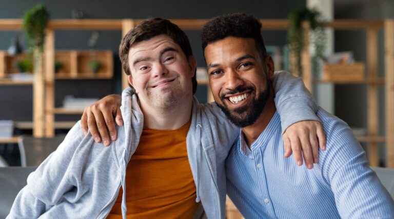 Two friends smiling with arms around each other indoors