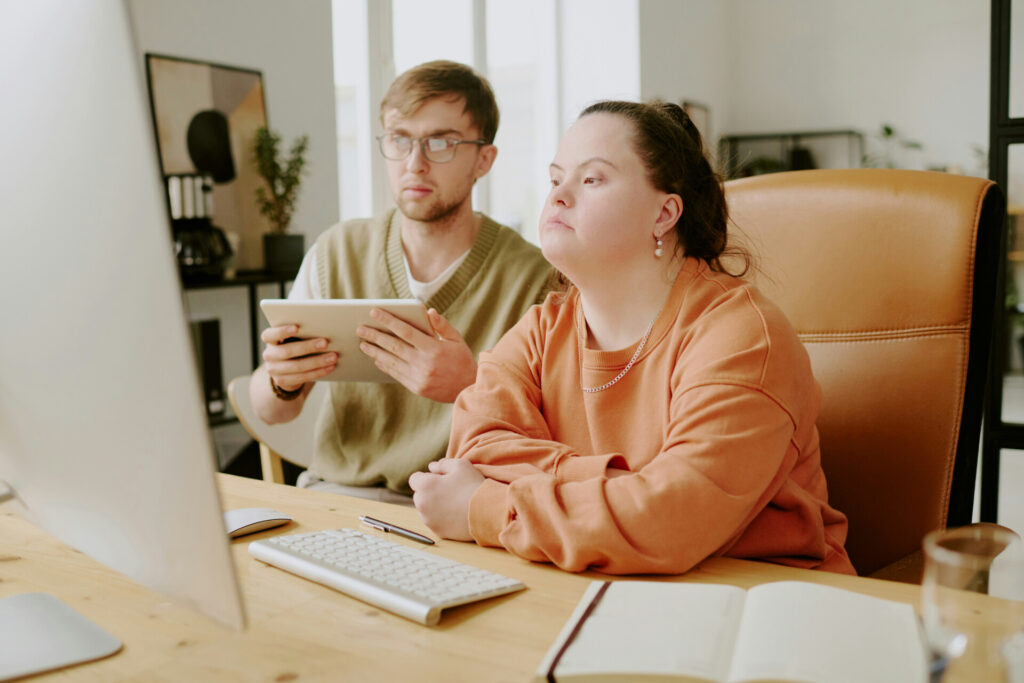 Two colleagues working at computer, one holding tablet