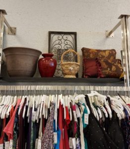 Clothing rack with shelf above holding flower vases, throw pillow, wicker basket, and home decor