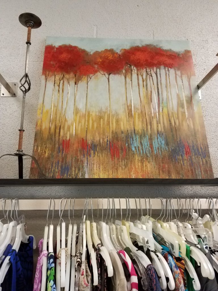 Painting of red trees on display above clothing rack at Ohio Valley Goodwill