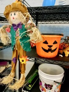 Stuffed scarecrow doll on a shelf with an orange jackolantern plastic bucket.