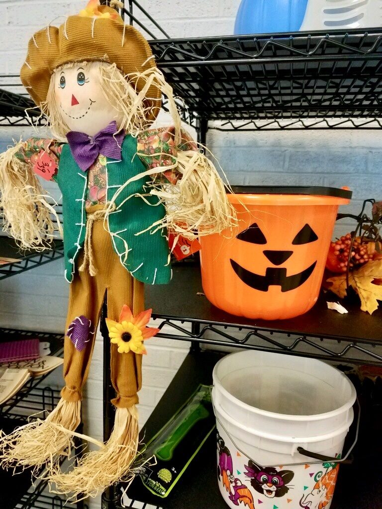 Stuffed scarecrow doll on a shelf with an orange jackolantern plastic bucket. 