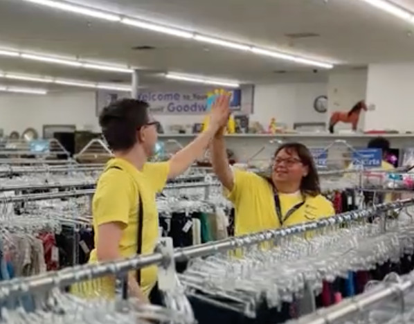Two employees high-fiving in thrift store aisle