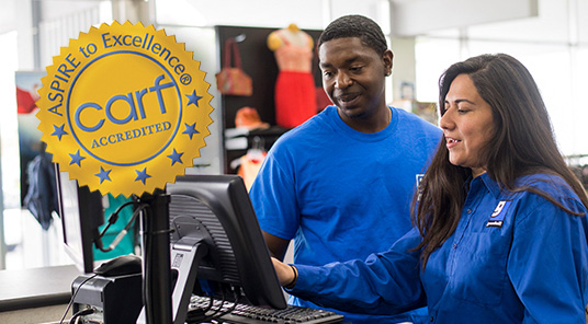 Two employees working at computer with CARF Accredited badge