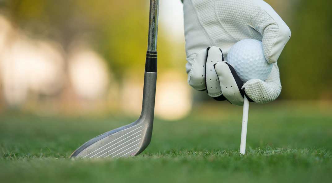 Golfer placing ball on tee with iron club