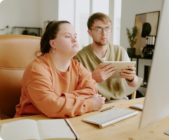 Two coworkers working together at desk with computer and tablet