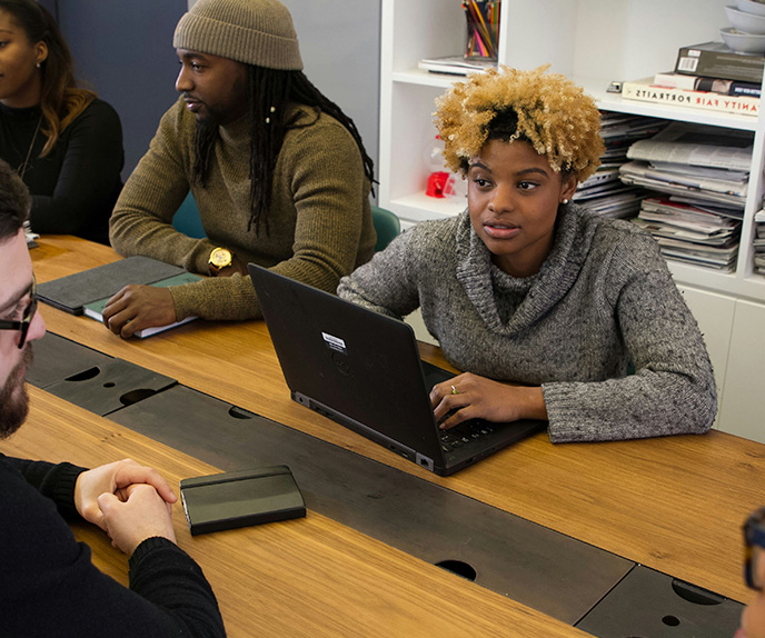 Team meeting with colleagues using laptops at table